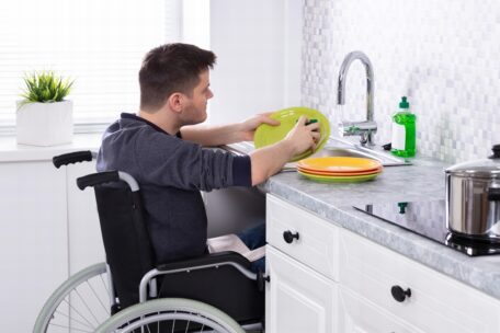 Man using his wheelchair in a SDA home which has cut outs under sinks.