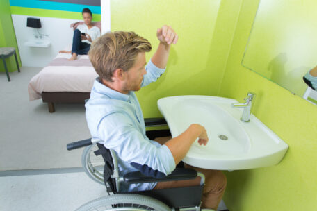 a man at his medium term accommodation is using a sink which his wheelchair fits under