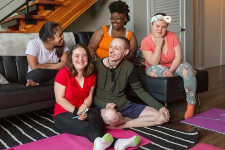 5 diverse people sitting on the couch or floor smiling and discussing the new NDIS Bill