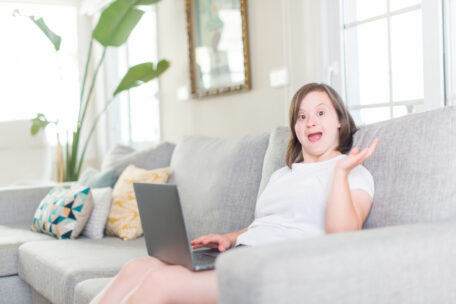 A young woman with Down Syndrome waves from her parents couch as she's finding it hard to get SDA for her home and living supports