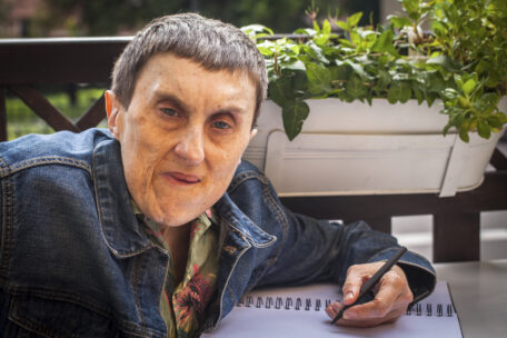A man with Cerebral Palsy sits down at his desk, writing his thoughts on SDA & home and living options