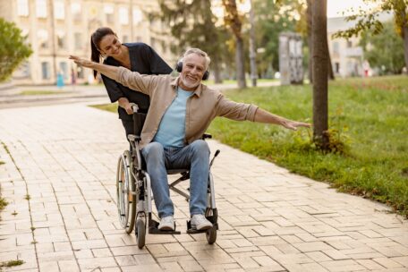 A man in a wheelchair with headphones on is pushed by his daughter