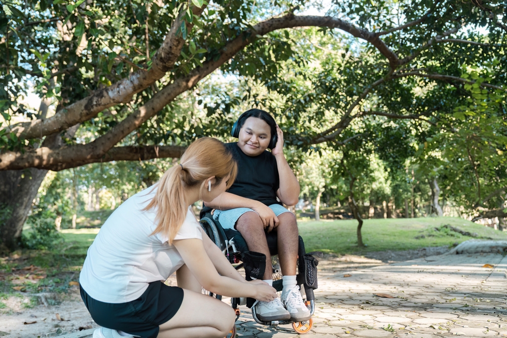 a woman is fussing over a mans shoes, the man is in a wheelchair. They are talking about a Change of Details and SDA for his NDIS plan