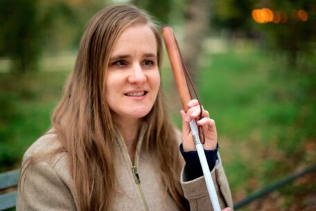 A blind woman sits on a park bench with her cane. She is thinking about her change of situation and SDA application