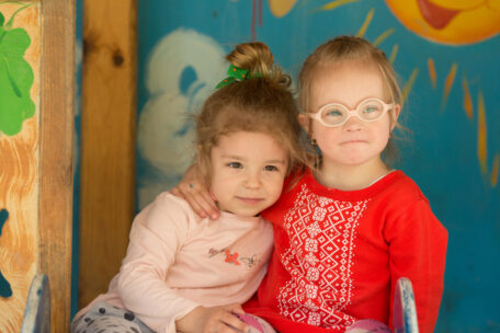 Two young girls with disabilities look at the camera in a nursery. Participant Service Guarantees for children are being kept up in 99% of cases. 