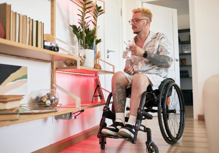 A man in a wheelchair is watering his plants at his home. He's thinking about the NDIS SDA quarterly report and how he loves his SDA home.