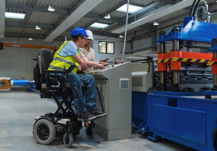a woman and man are in a manafacturing plant. The man is using a electric wheelchair. In the NDIS quarterly report q4 people with disabilities are more likely to have a job.