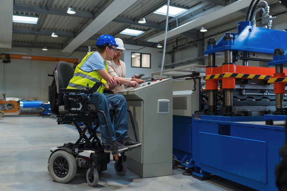 a woman and man are in a manafacturing plant. The man is using a electric wheelchair. In the NDIS quarterly report q4 people with disabilities are more likely to have a job.