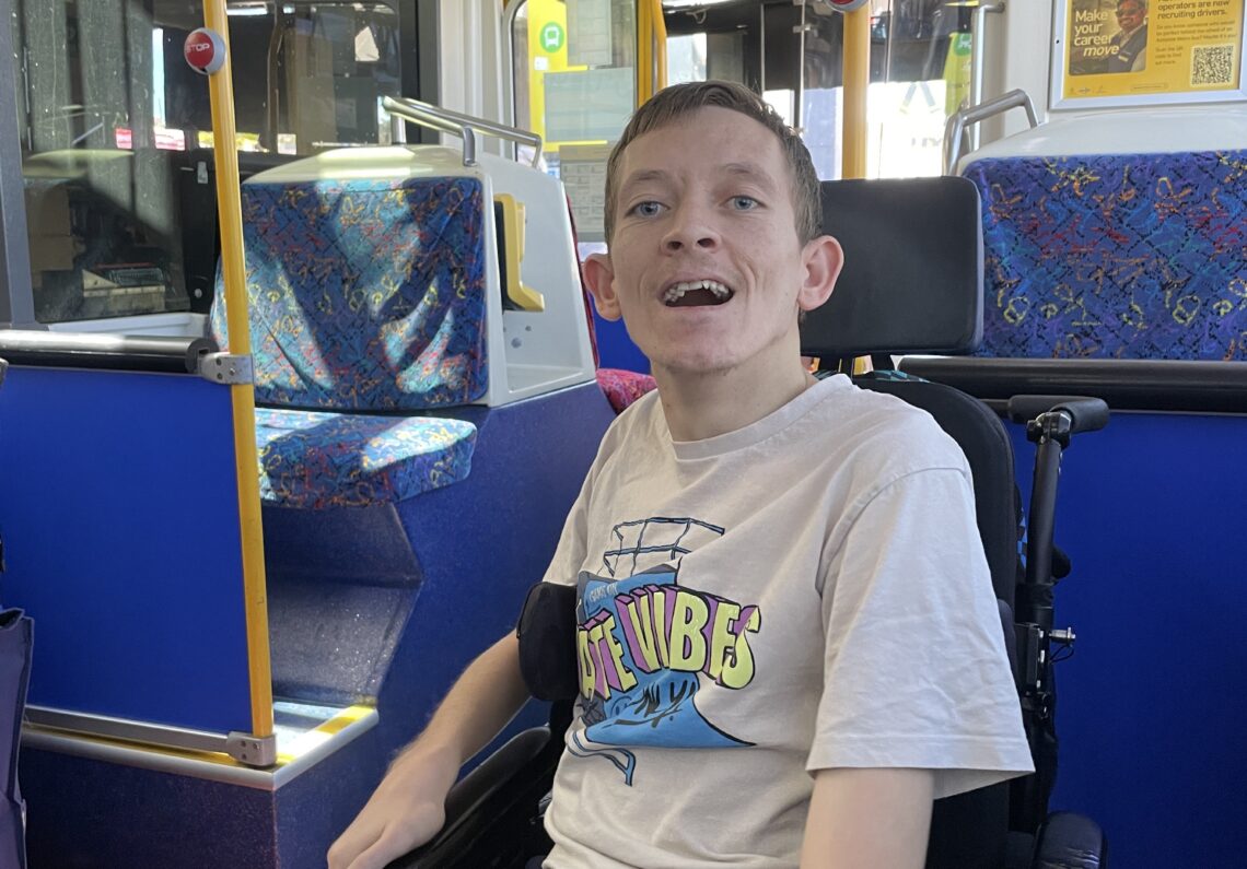 Ryans sits in his wheelchair on the bus. He's looking at the camera and smiling